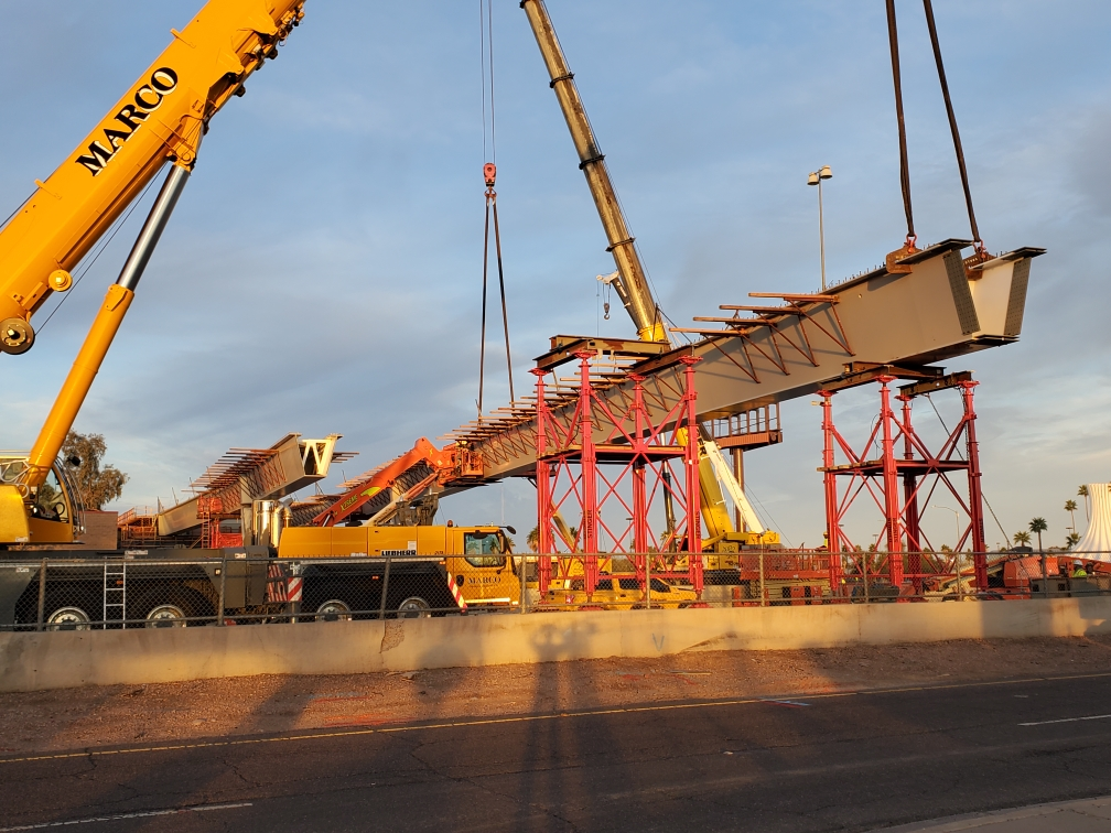 Construction Project Services involved in the construction of a bridge with cranes lifting large sections into place at sunset.