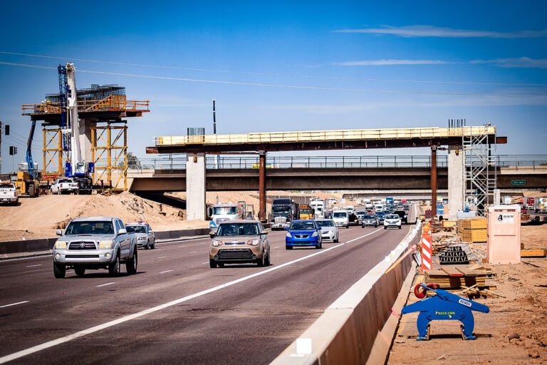 Construction of an overpass bridge above a busy highway, executed by Civil Engineering Services, with visible traffic and construction equipment.